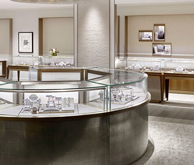 Classic crystal chandeliers highlight focal points within the room, drawing attention to central shopping moments, while a wood floor perimeter guides shoppers through the store past mirrored surfaces to create a natural illusion with sparkle and reflectivity.