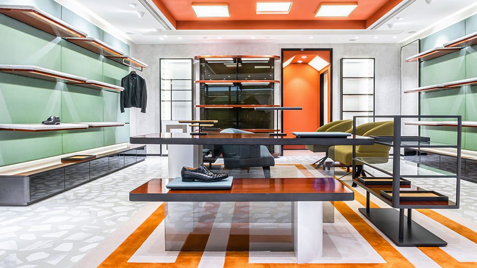 Shoes are arranged on a series of upholstered shelves over the pale green wall. The fabric of the shelves adds a soft contrast to the environment with a special touch and bespoke elegance.