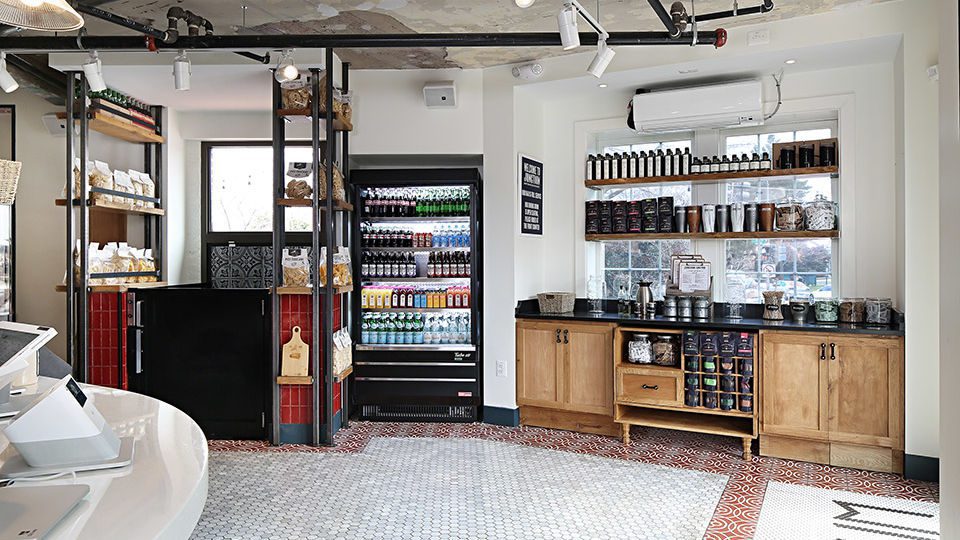 At the front sits the main bakery counter and cozy banquette, where patrons can pick up a coffee and fresh pastries. Enameled countertops and reclaimed wood sourced by the owner defines the bakery and coffee zone. Retail shelving flanking the entry to the bar and main dining space creates a threshold from pick-up/bakery to restaurant and bar.