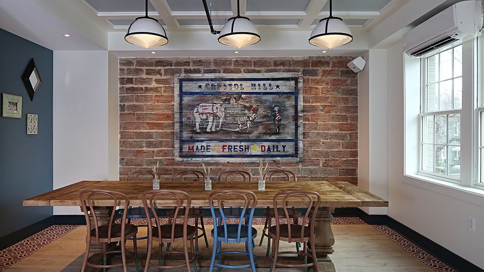 At the back space, the community table provides a cozy nook with a backdrop of original exposed brick, and a hand-painted mural by artist Selene Mendez.