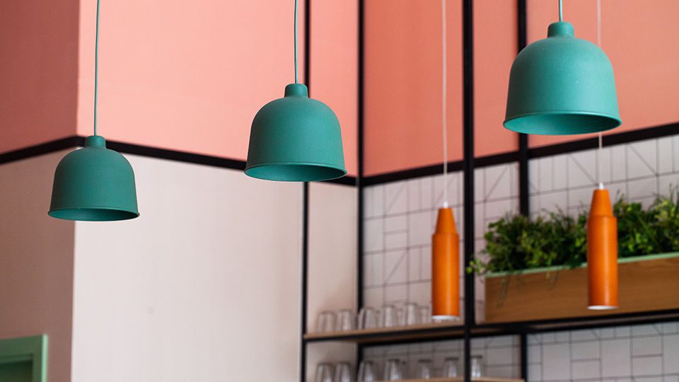 The terracotta wall and pendant lighting that are in line with the pinks and green add warmth. The pendant lights frame the central communal table and the perimeter banquette seating while the ones on the walls tie the elements together and create variation.