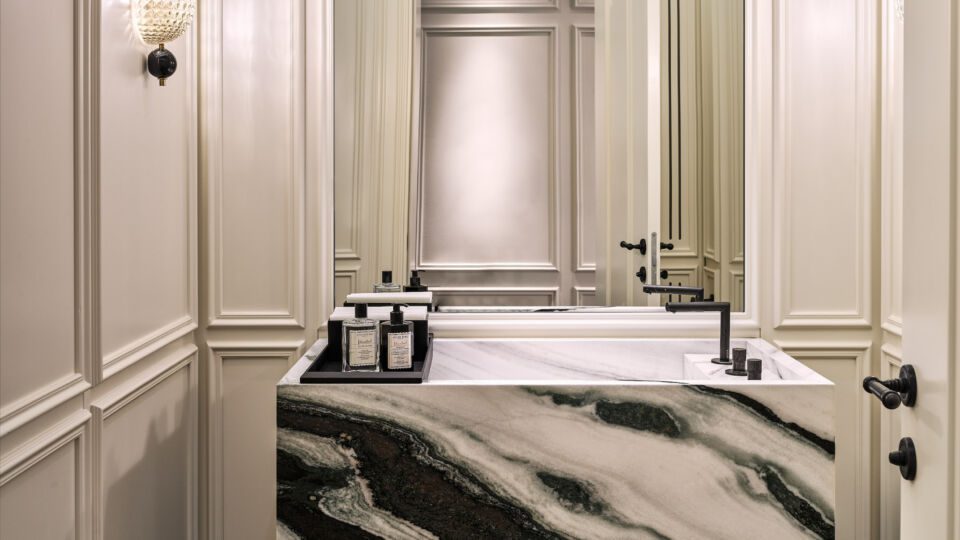 For the bathroom in the showroom, marquetry flooring has been used, while walls are clad in wooden panels. The sink is custom-made from a black and white Bianco Lasa Vena Nera marble block.