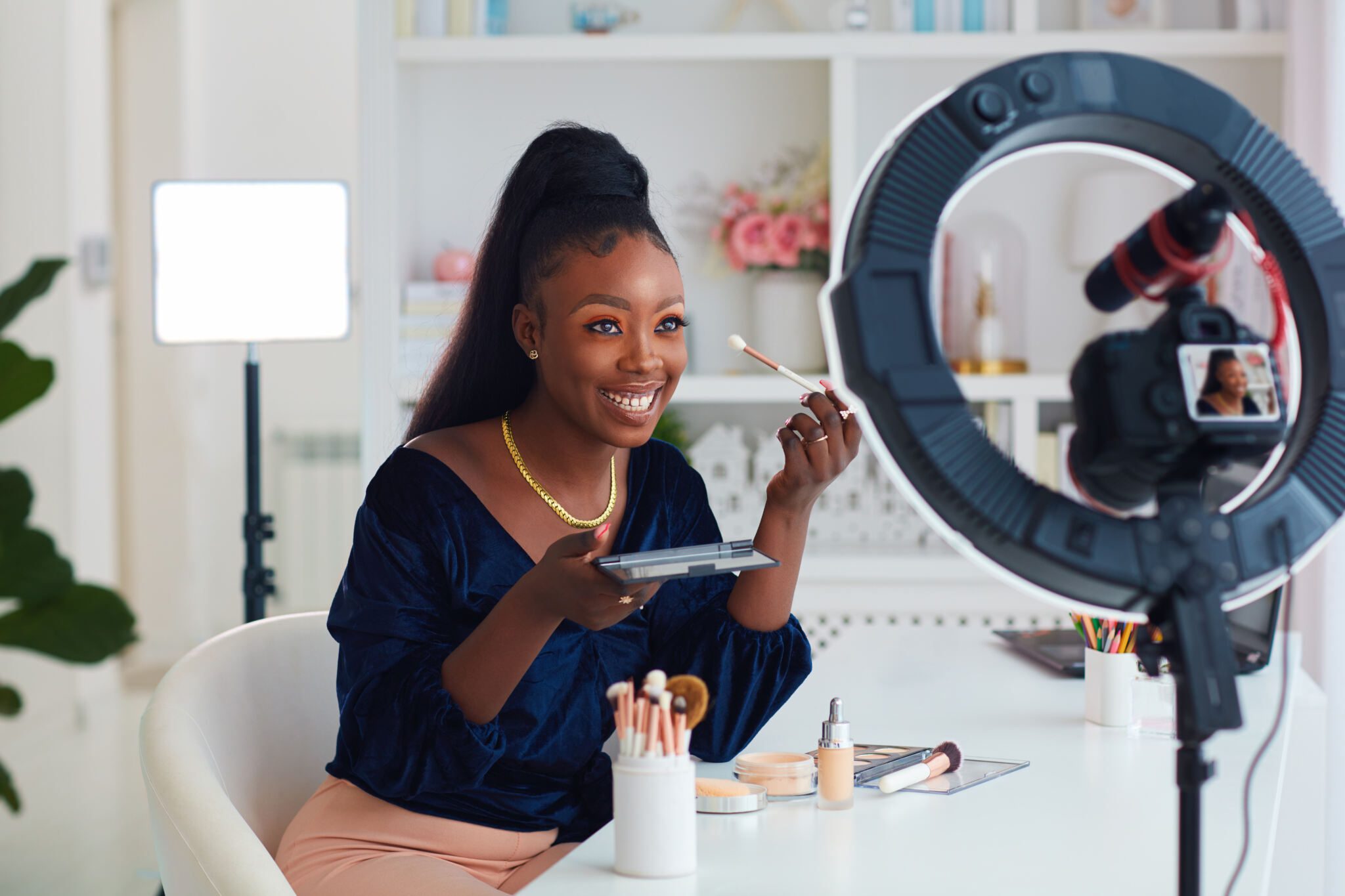 Happy African American woman putting on makeup during a live shopping tutorial.
