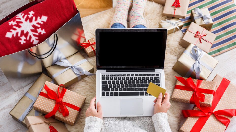 Person shopping on a laptop with holiday packages surrounding them