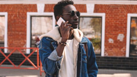 An African American Gen Z consumer outside talking on a smartphone. He's outside on a sunny day, looking into the distance.