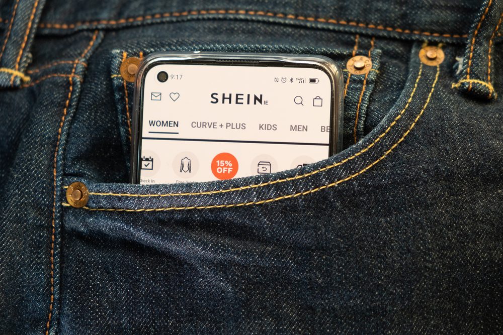 An image of a smartphone with the SHEIN ecommerce site on it. The smartphone is in a pocket for a pair of jeans.