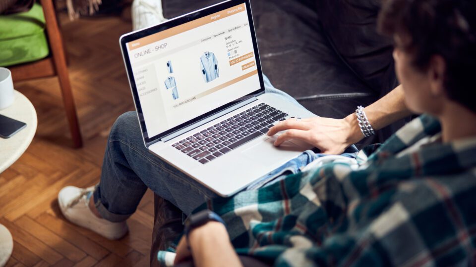 Close up of guy with laptop on his laps buying shirt in online shop stock photo