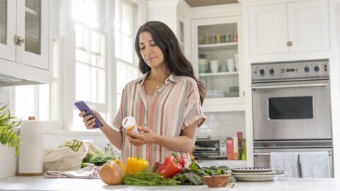 A woman using her CVS Health app during dinner prep.