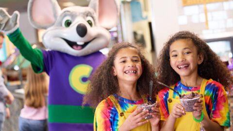 Kids at a Chuck E Cheese with character in the background.