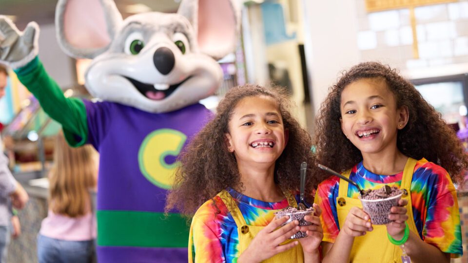 Kids at a Chuck E Cheese with character in the background.
