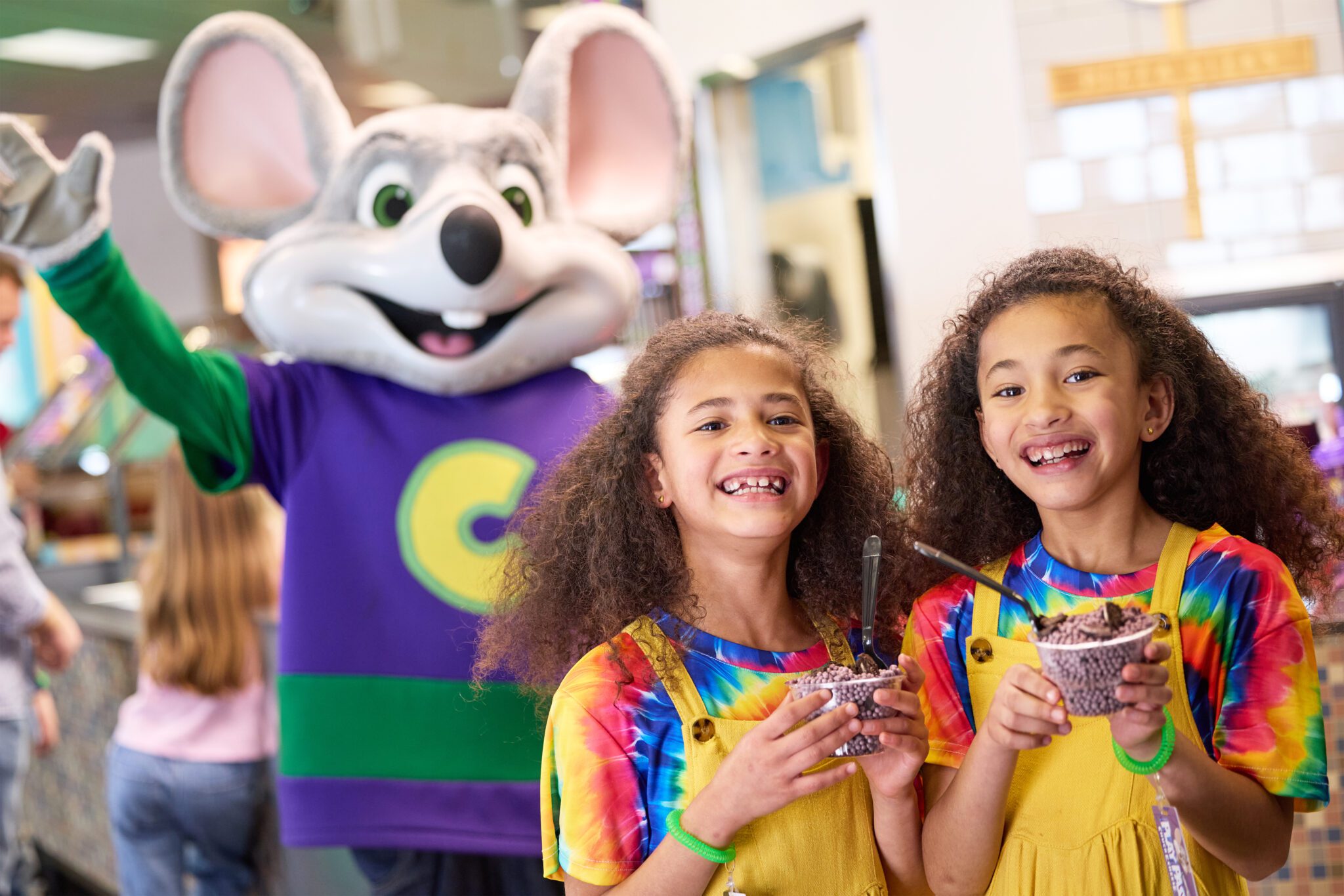 Kids at a Chuck E Cheese with character in the background.